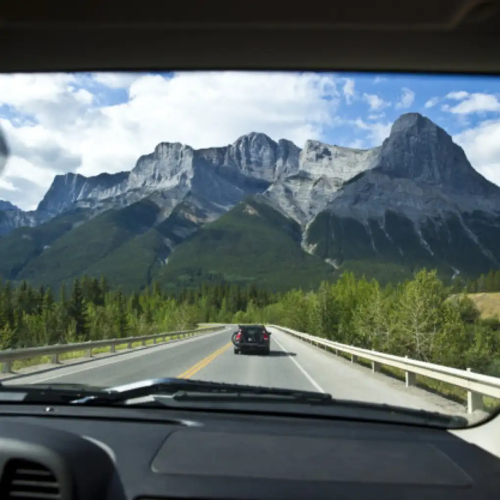 Cars drive along a highway toward a mountain peak