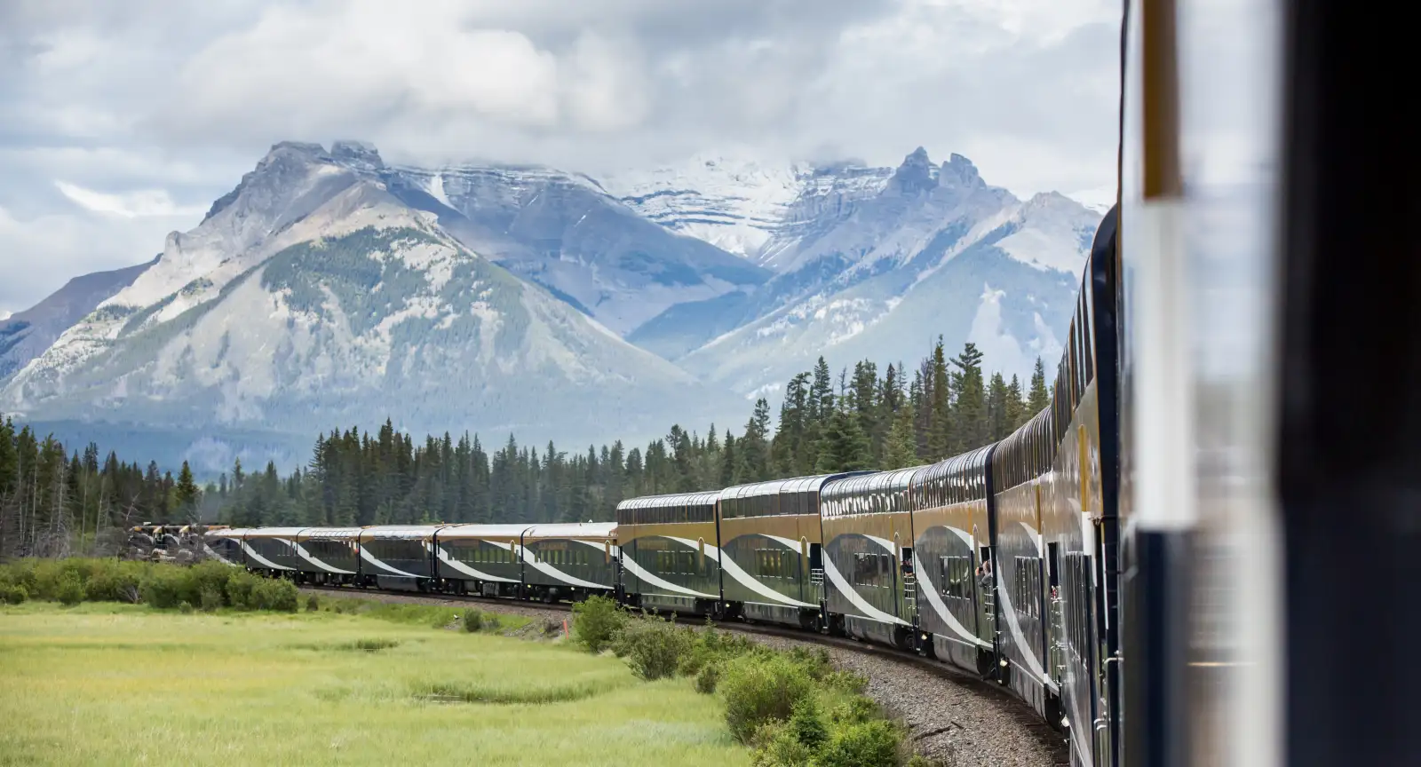 Man photographs crystal clear blue river through a Rocky Mountaineer train window