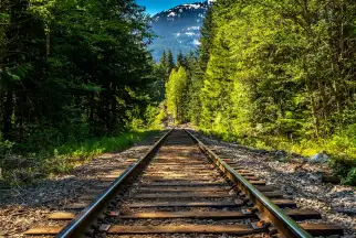 Railway tracks cutting through a lush green forest in Canada with soaring mountain peaks in the distance