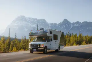 Cruise Canada motorhome drives along in front of a rocky mountain scene