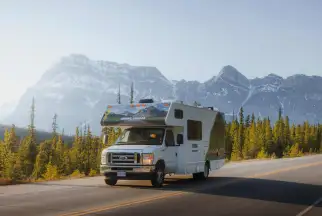 A Cruise Canada RV travelling on a scenic road in Canada with snow-capped mountain peaks on the background