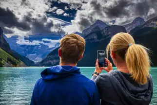 A woman takes a picture of a scenic turquoise lake in the Canadian Rockies