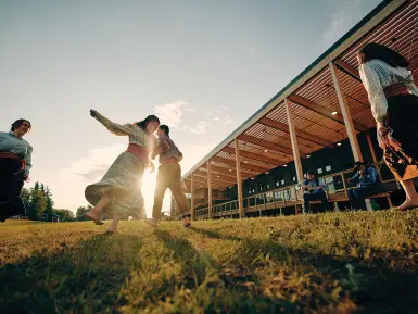 People dance in traditional dress in front of the setting sun