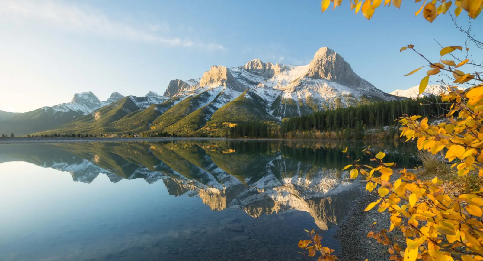a snowy mountain peak is reflected in a lake below