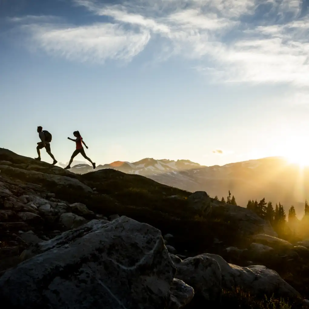 A couple hike up a picturesque mountain slope in Whistler as the sun rises behind them
