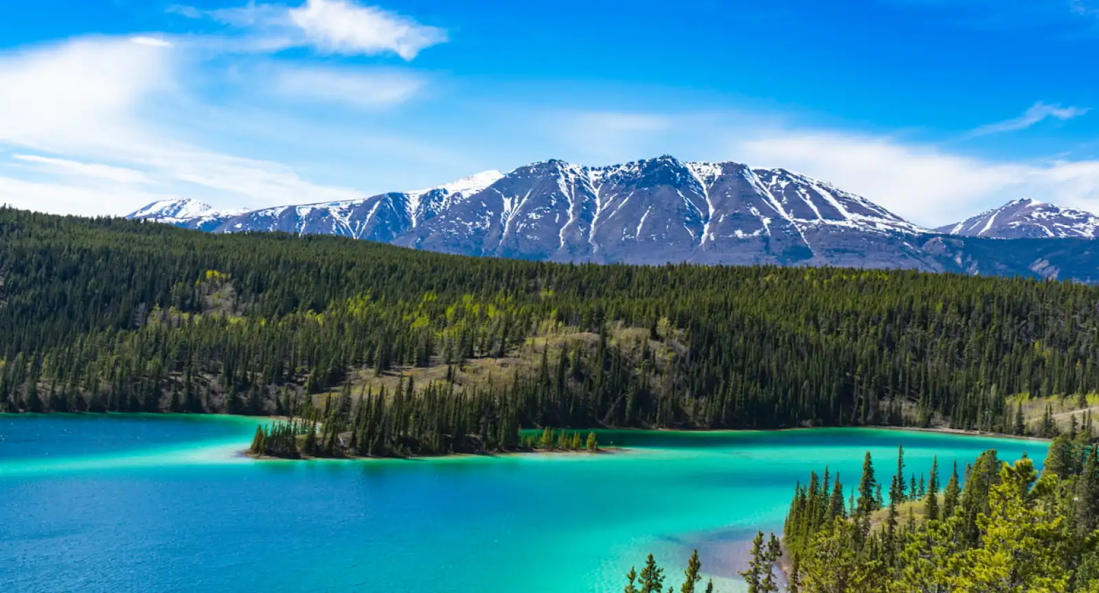 Turquoise lake in front of snowy mountain scene in Yukon, Canada