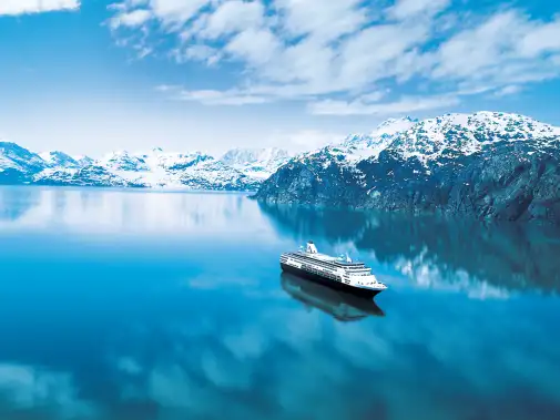 The tranquil blue Inside Passage waterway, surrounded by snow-capped mountains under a bright sky with scattered clouds.