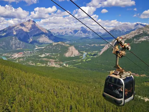 A gondola ascends offering passengers a stunning view of majestic peaks of Sulphur Mountain, Banff in the distance under a clear sky.